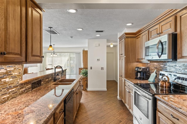 kitchen with brown cabinets, visible vents, appliances with stainless steel finishes, light wood-style floors, and a sink