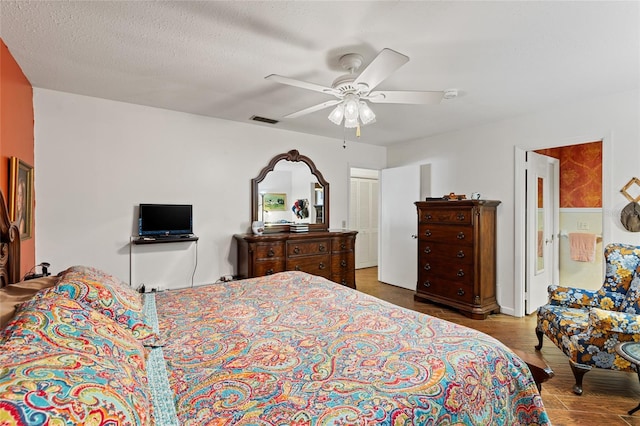 bedroom with a textured ceiling, ceiling fan, wood finished floors, and visible vents