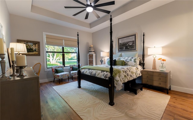 bedroom with wood finished floors, baseboards, and a raised ceiling