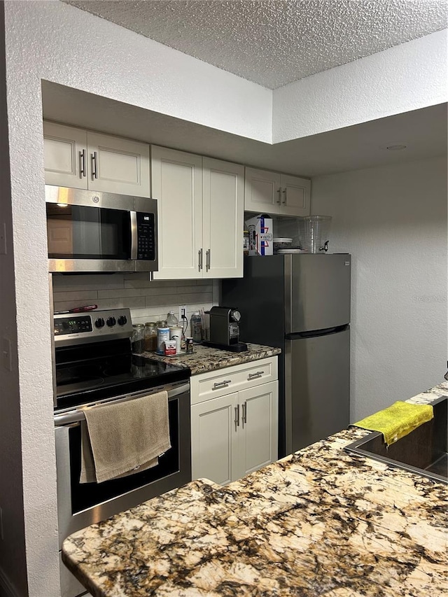 kitchen featuring a textured ceiling, a textured wall, white cabinetry, appliances with stainless steel finishes, and backsplash