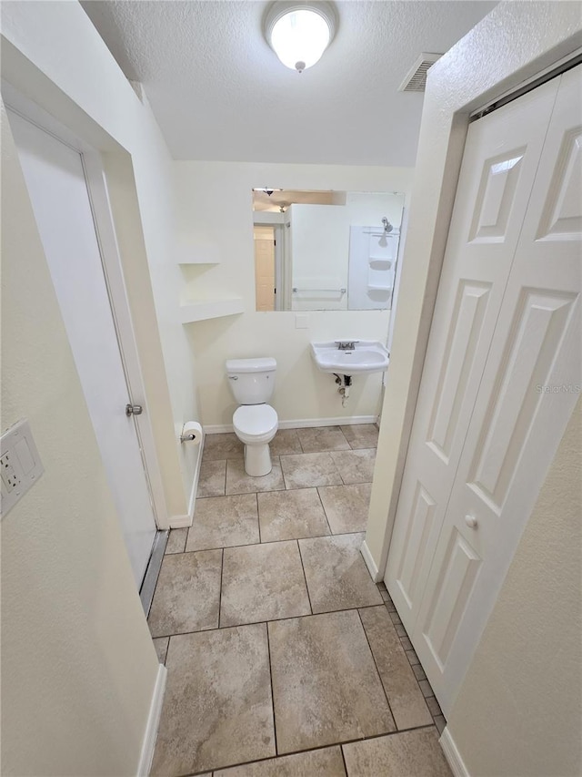 bathroom featuring tile patterned floors, a textured ceiling, a sink, toilet, and visible vents