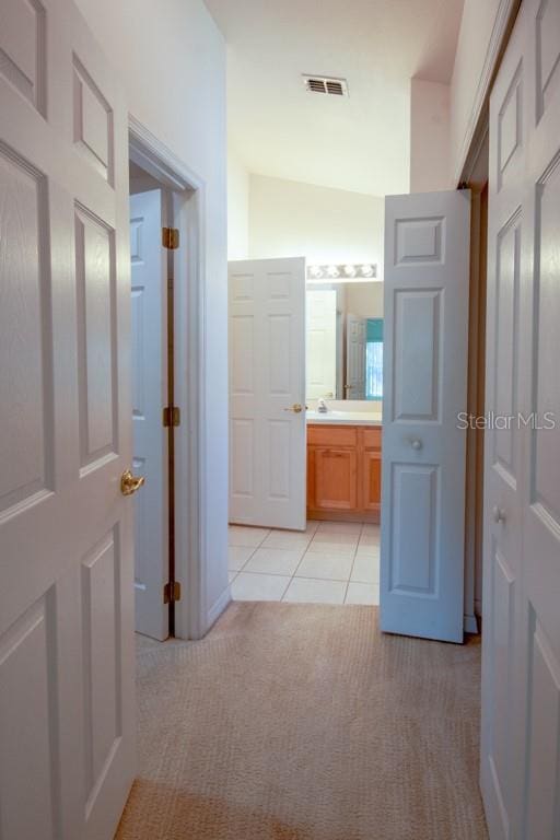 hallway with light carpet, light tile patterned floors, a sink, and visible vents