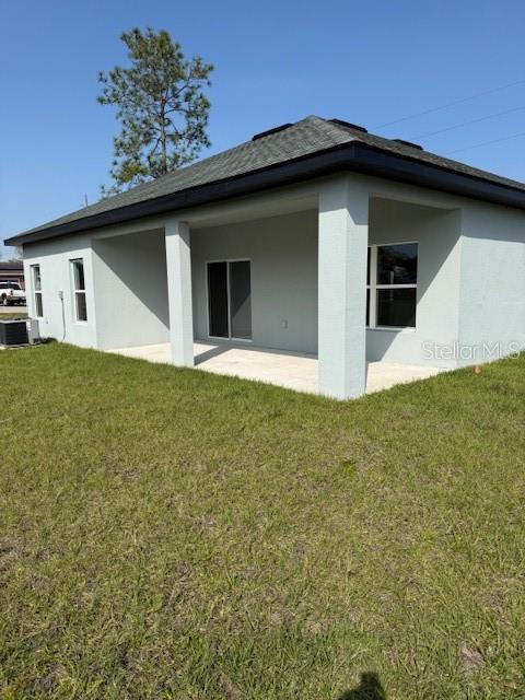 back of property with a patio area, stucco siding, central AC, and a yard