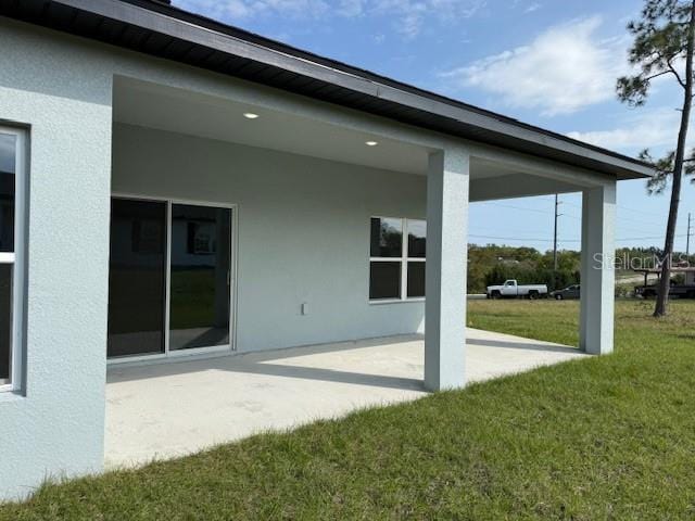 rear view of house featuring a patio, a lawn, and stucco siding