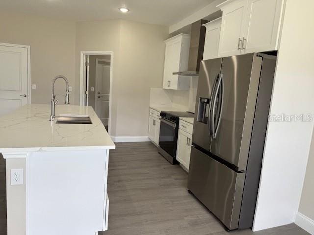 kitchen featuring a center island with sink, a sink, stainless steel fridge, wall chimney range hood, and black electric range oven