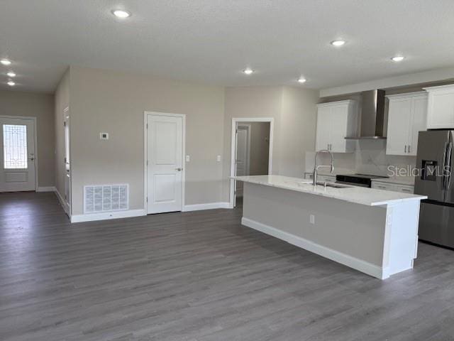 kitchen featuring visible vents, a sink, stainless steel fridge, wall chimney exhaust hood, and a kitchen island with sink