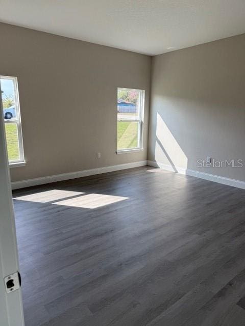 spare room with a healthy amount of sunlight, baseboards, and dark wood-style flooring