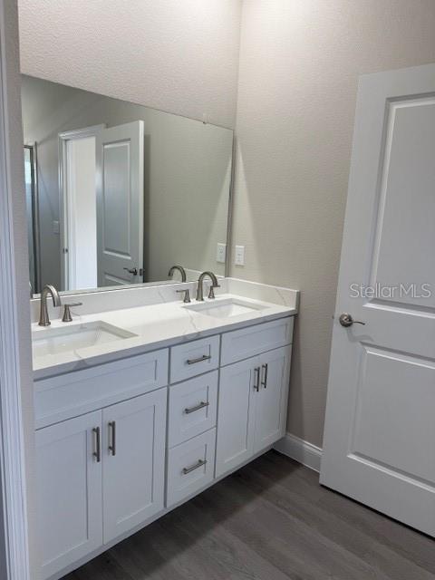 full bath with double vanity, wood finished floors, baseboards, and a sink