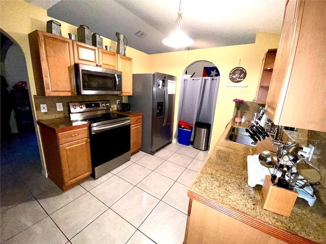 kitchen featuring arched walkways, appliances with stainless steel finishes, light tile patterned floors, and a sink