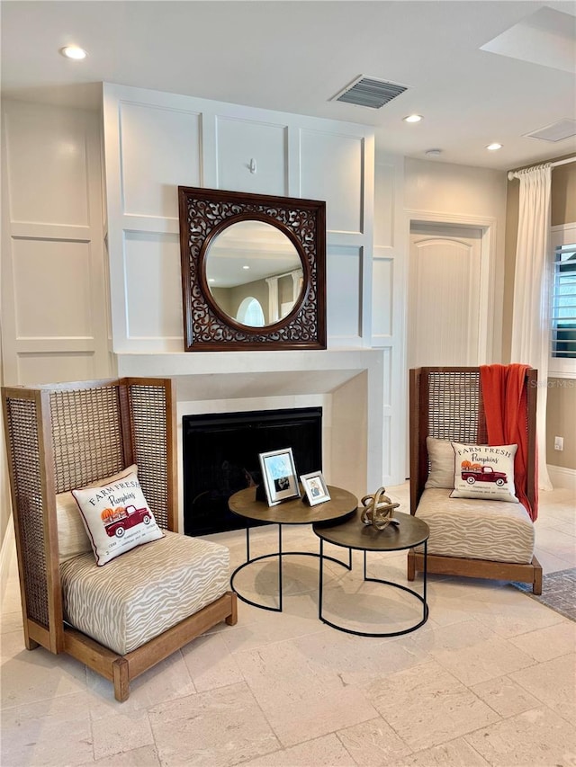 sitting room featuring visible vents, stone tile flooring, recessed lighting, a fireplace, and a decorative wall