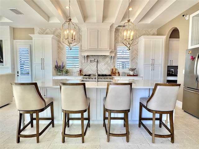 kitchen with a center island with sink, stone tile floors, decorative backsplash, freestanding refrigerator, and a notable chandelier