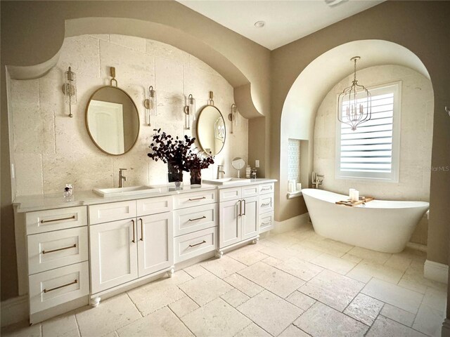 bathroom featuring double vanity, a soaking tub, stone tile floors, and a sink