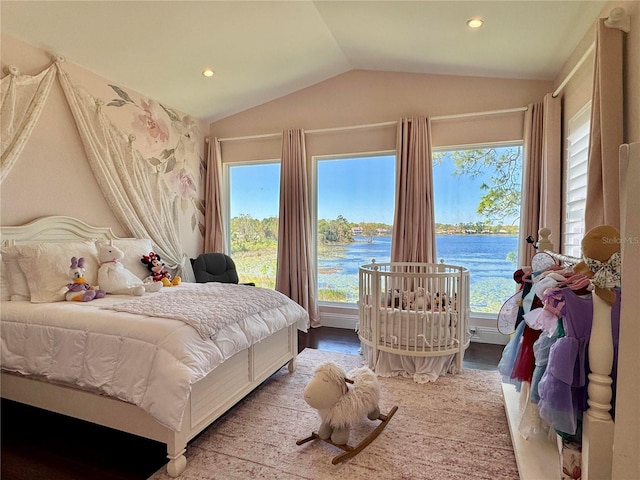 bedroom with multiple windows, lofted ceiling, wood finished floors, and a water view