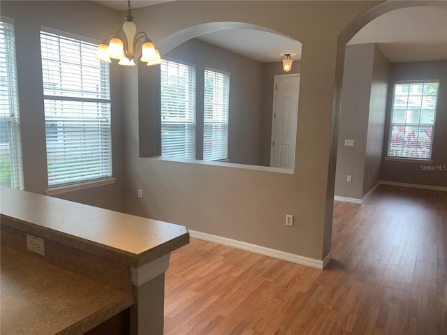 unfurnished dining area featuring arched walkways, a chandelier, light wood-type flooring, and baseboards