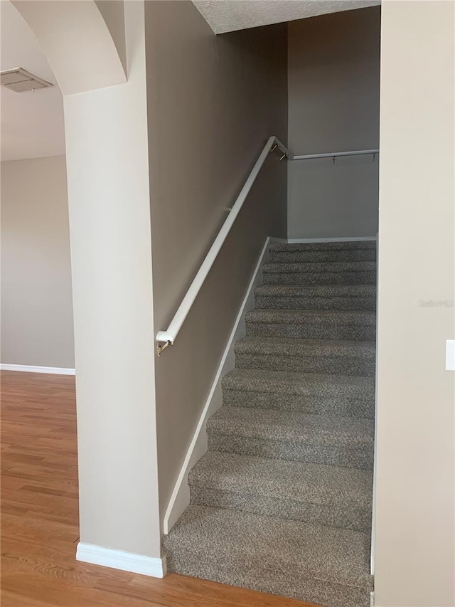 staircase with visible vents, baseboards, and wood finished floors