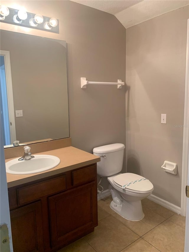 bathroom featuring toilet, tile patterned flooring, baseboards, vanity, and vaulted ceiling