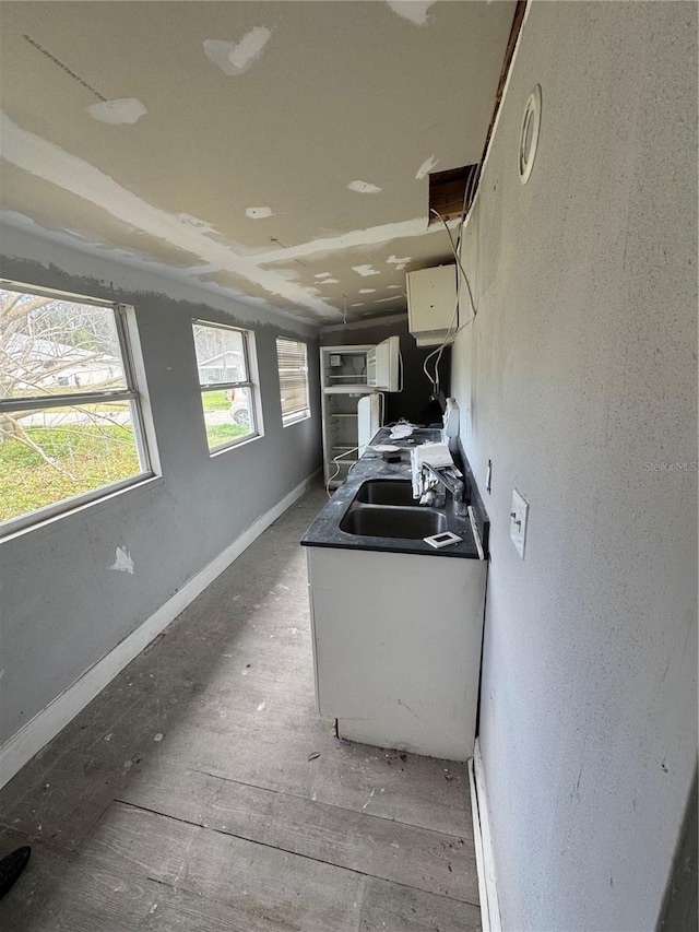 kitchen featuring white cabinets, baseboards, and a sink