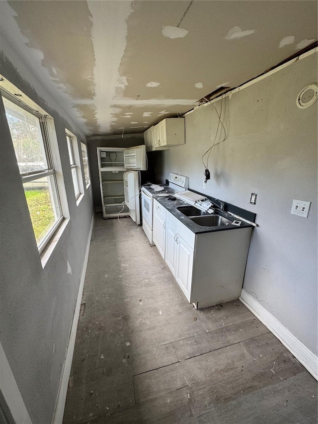 kitchen with a sink, baseboards, white cabinets, and electric stove