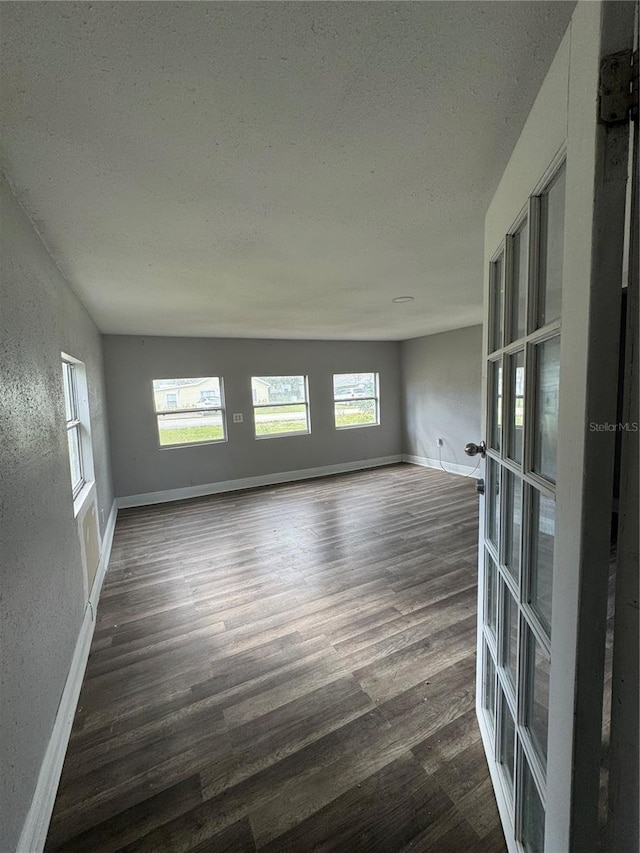 unfurnished room with dark wood-type flooring, a textured ceiling, french doors, baseboards, and a textured wall