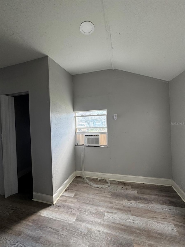 spare room with lofted ceiling, cooling unit, wood finished floors, and baseboards