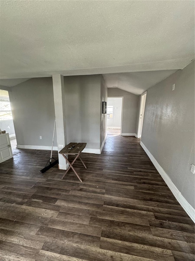 empty room featuring lofted ceiling, baseboards, dark wood-style flooring, and a textured ceiling