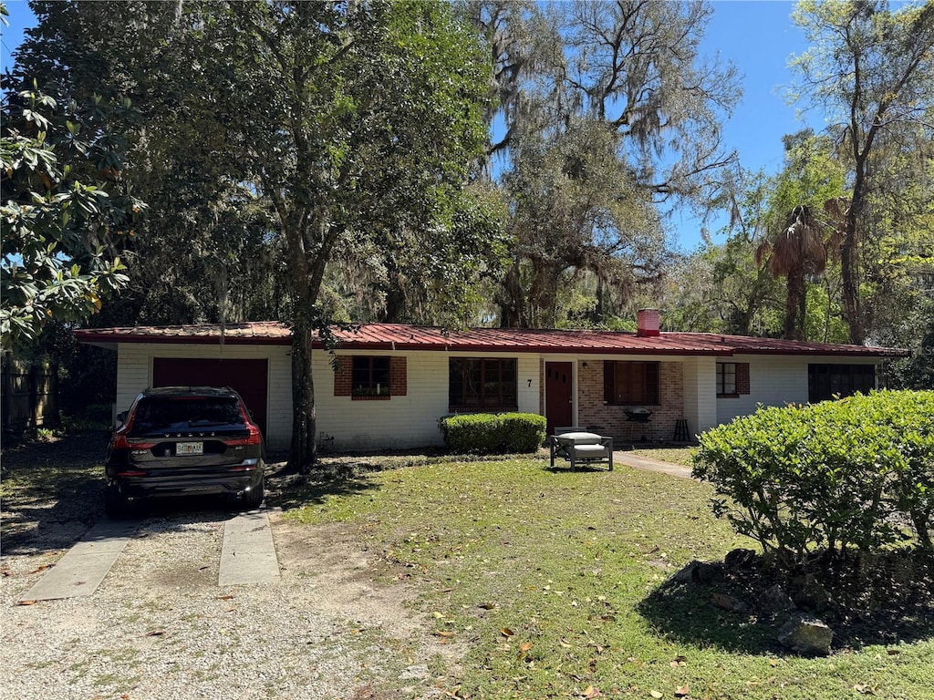 ranch-style home featuring an attached garage, concrete driveway, a front lawn, brick siding, and metal roof