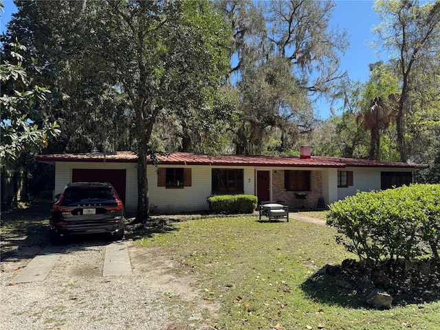 ranch-style home featuring an attached garage, concrete driveway, a front lawn, brick siding, and metal roof