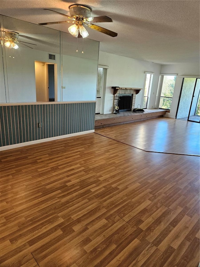 8744 54th Ave W Unit 8744, Bradenton, FL 34210 - unfurnished living room featuring wood finished floors, ceiling fan, a textured ceiling, a brick fireplace, and a wainscoted wall