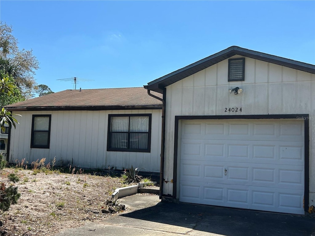 ranch-style house with concrete driveway, a garage, and roof with shingles