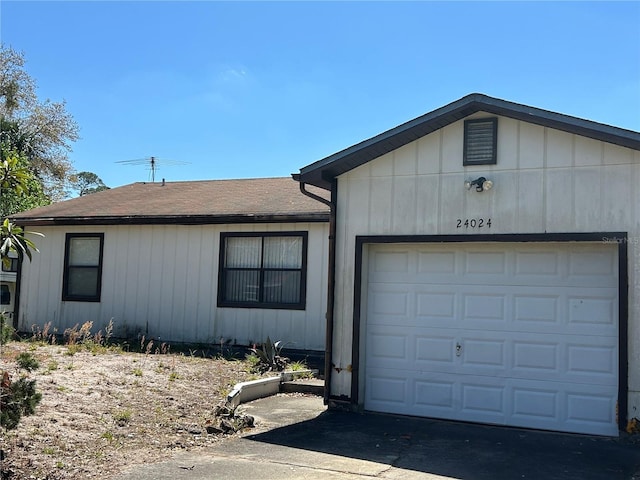 ranch-style house with concrete driveway, a garage, and roof with shingles