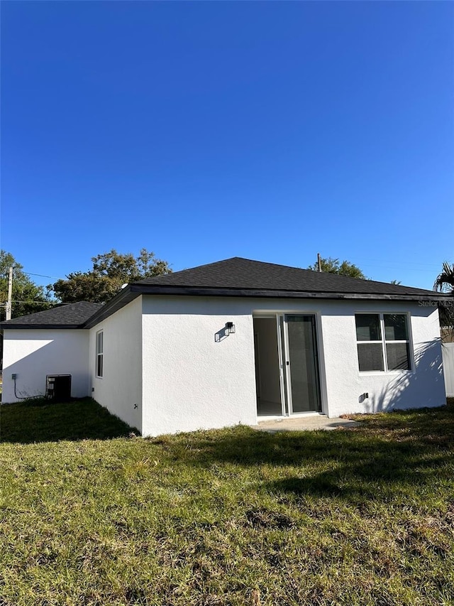 back of house with stucco siding, a yard, and central AC unit