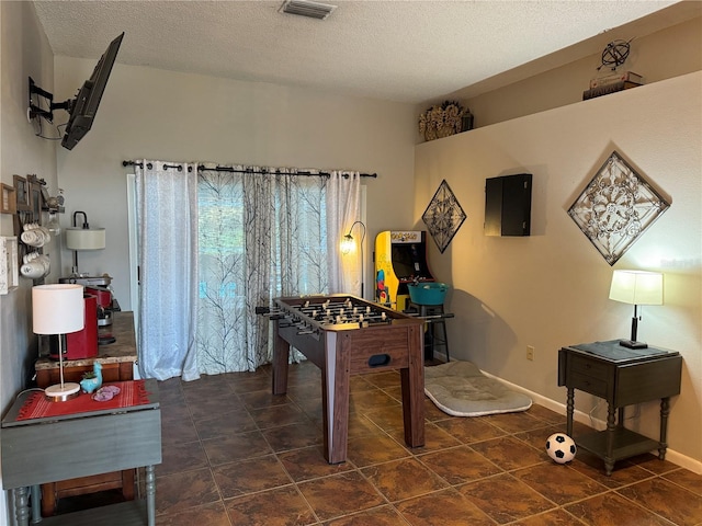 recreation room with baseboards, visible vents, and a textured ceiling