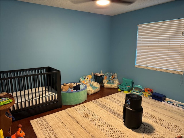 bedroom with ceiling fan, a textured ceiling, and a nursery area