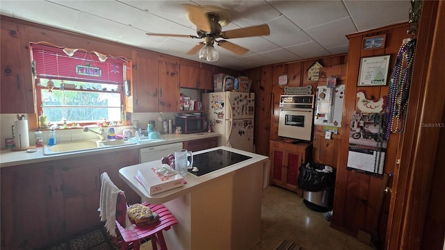 kitchen with white appliances, ceiling fan, a sink, light countertops, and wood walls