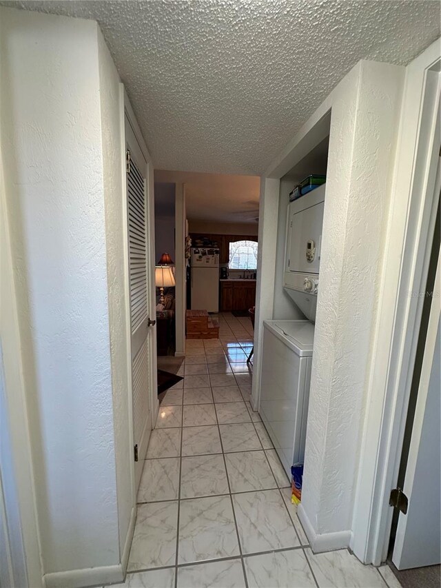 clothes washing area with a textured ceiling, marble finish floor, stacked washing maching and dryer, and laundry area