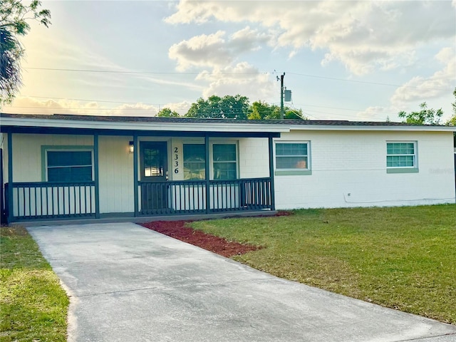 single story home featuring a front lawn, concrete block siding, covered porch, and concrete driveway