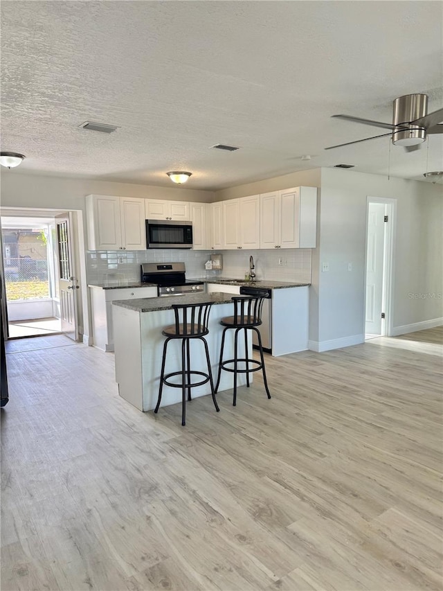 kitchen with white cabinetry, a kitchen bar, backsplash, and stainless steel appliances