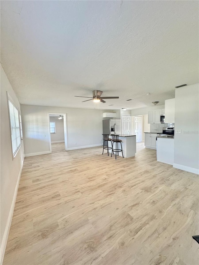 unfurnished living room with a ceiling fan, light wood-style flooring, a textured ceiling, and visible vents