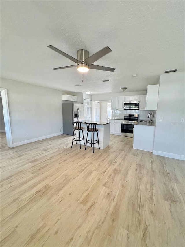 kitchen featuring white cabinetry, a kitchen breakfast bar, light wood finished floors, and appliances with stainless steel finishes