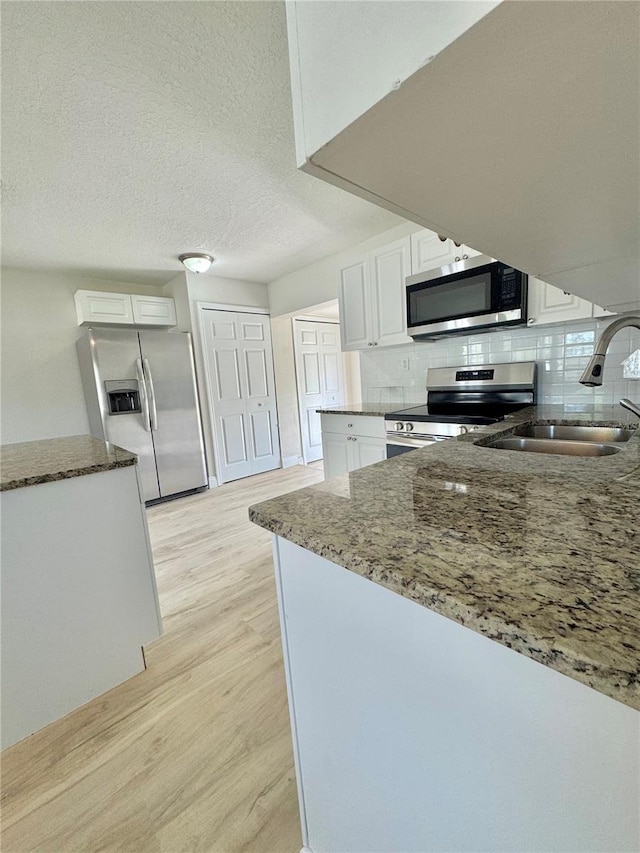 kitchen featuring stainless steel appliances, a sink, stone countertops, light wood finished floors, and white cabinets