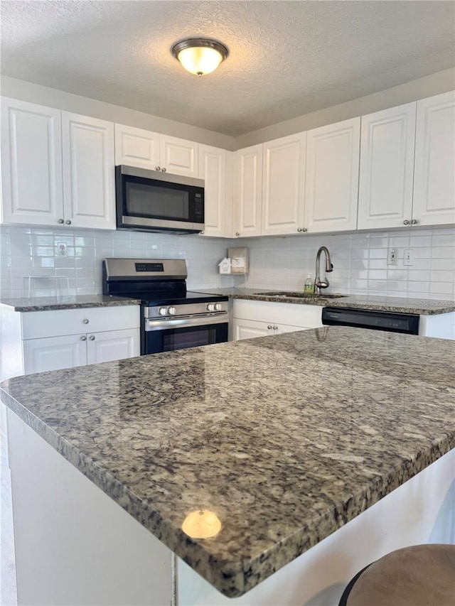 kitchen with white cabinets, stainless steel appliances, dark stone counters, tasteful backsplash, and a sink