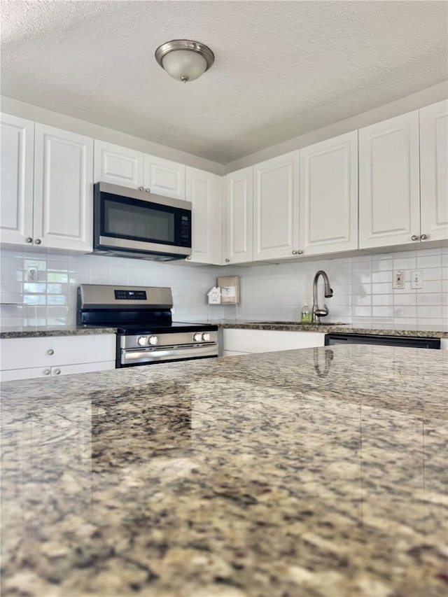 kitchen with backsplash, white cabinets, and appliances with stainless steel finishes