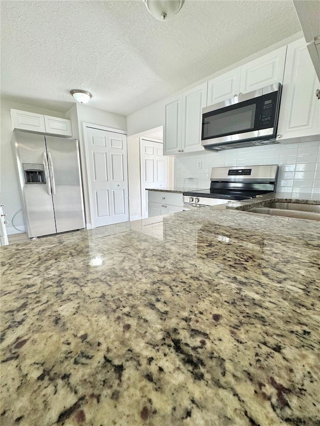 kitchen featuring a textured ceiling, light stone countertops, tasteful backsplash, appliances with stainless steel finishes, and white cabinetry