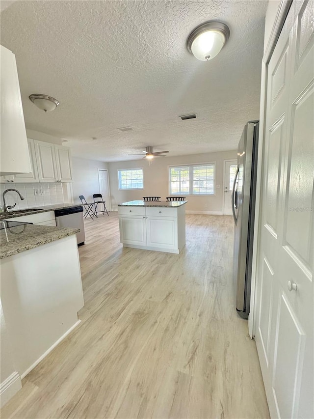 kitchen featuring visible vents, light wood finished floors, appliances with stainless steel finishes, white cabinetry, and a sink