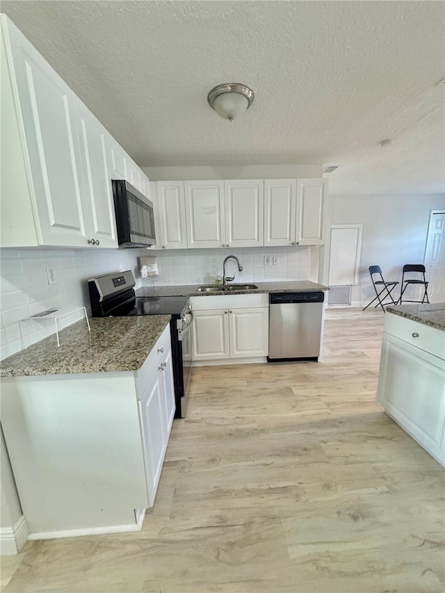 kitchen with white cabinetry, a sink, light wood-type flooring, and appliances with stainless steel finishes