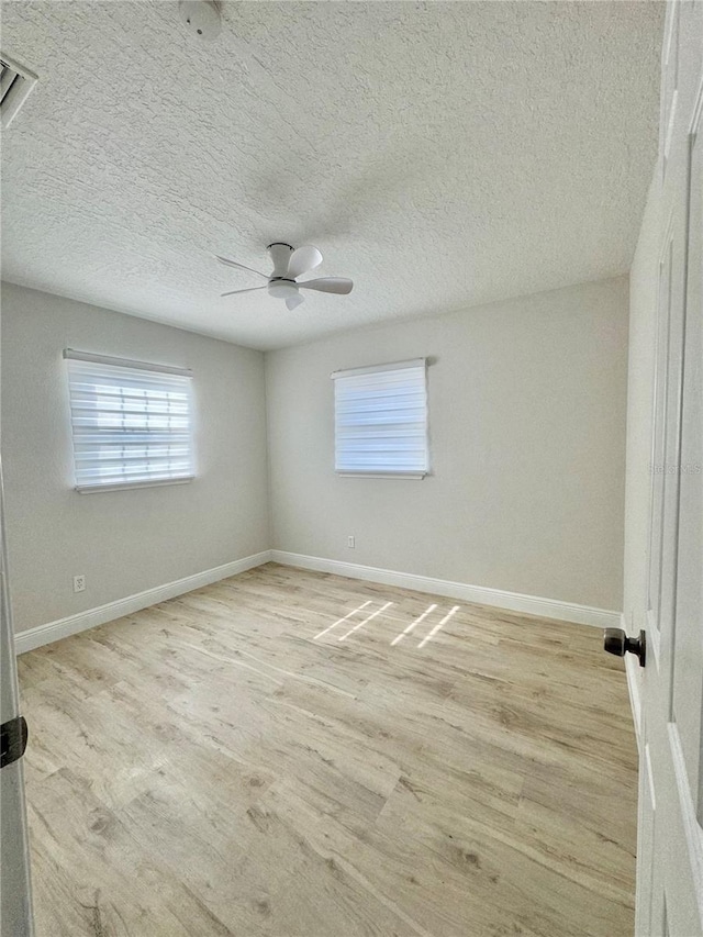 empty room featuring a textured ceiling, baseboards, light wood-style floors, and a ceiling fan
