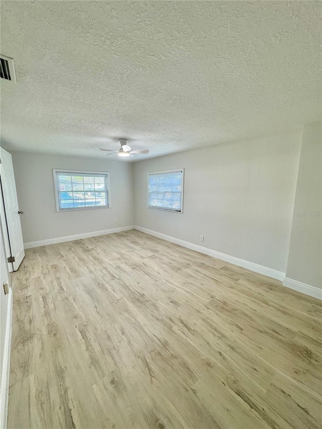 unfurnished room with a textured ceiling, light wood-type flooring, baseboards, visible vents, and ceiling fan