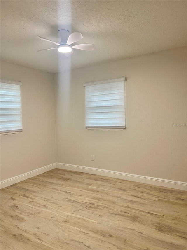 empty room with baseboards, a textured ceiling, and light wood-style flooring