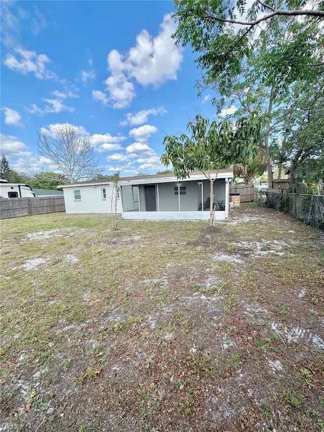 rear view of house featuring a fenced backyard, a sunroom, and a yard