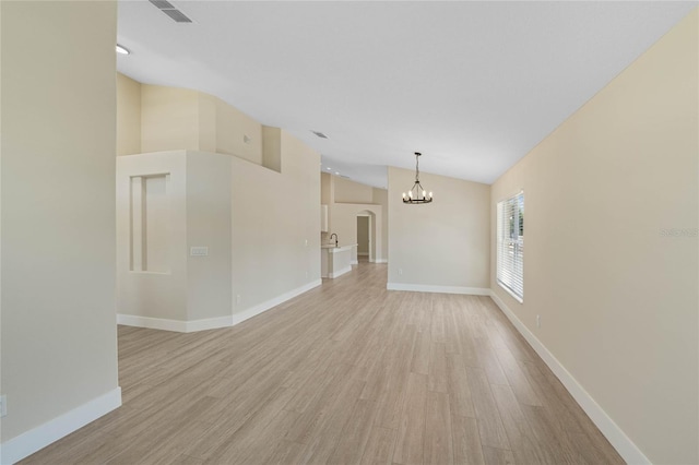 unfurnished room featuring light wood finished floors, a chandelier, baseboards, lofted ceiling, and visible vents